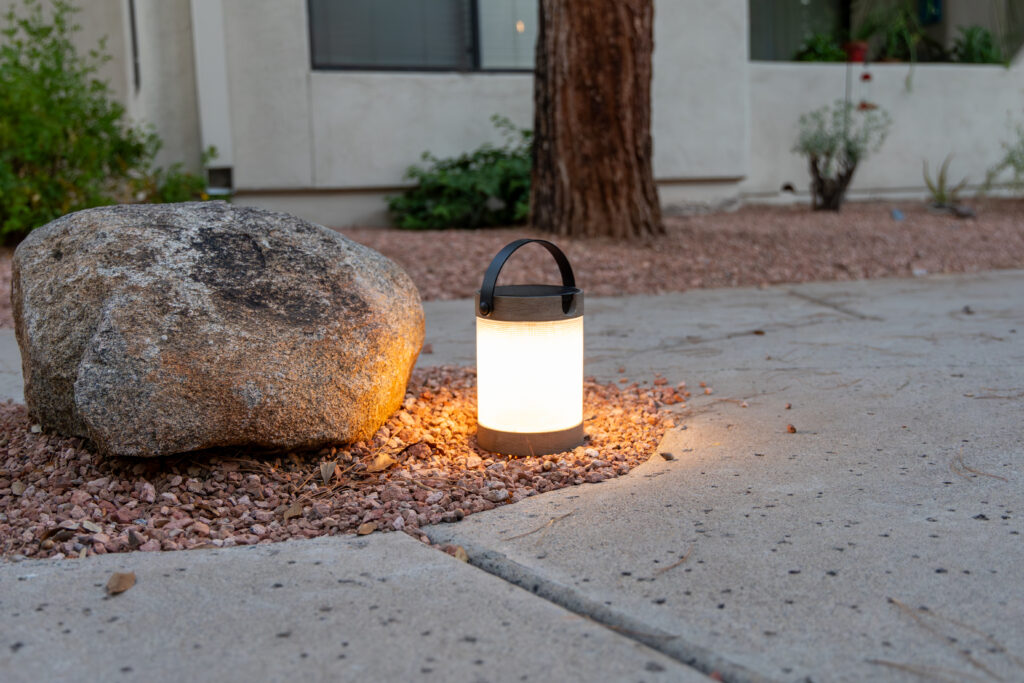 modern solar powered lantern is lit up in the gravel near a rock